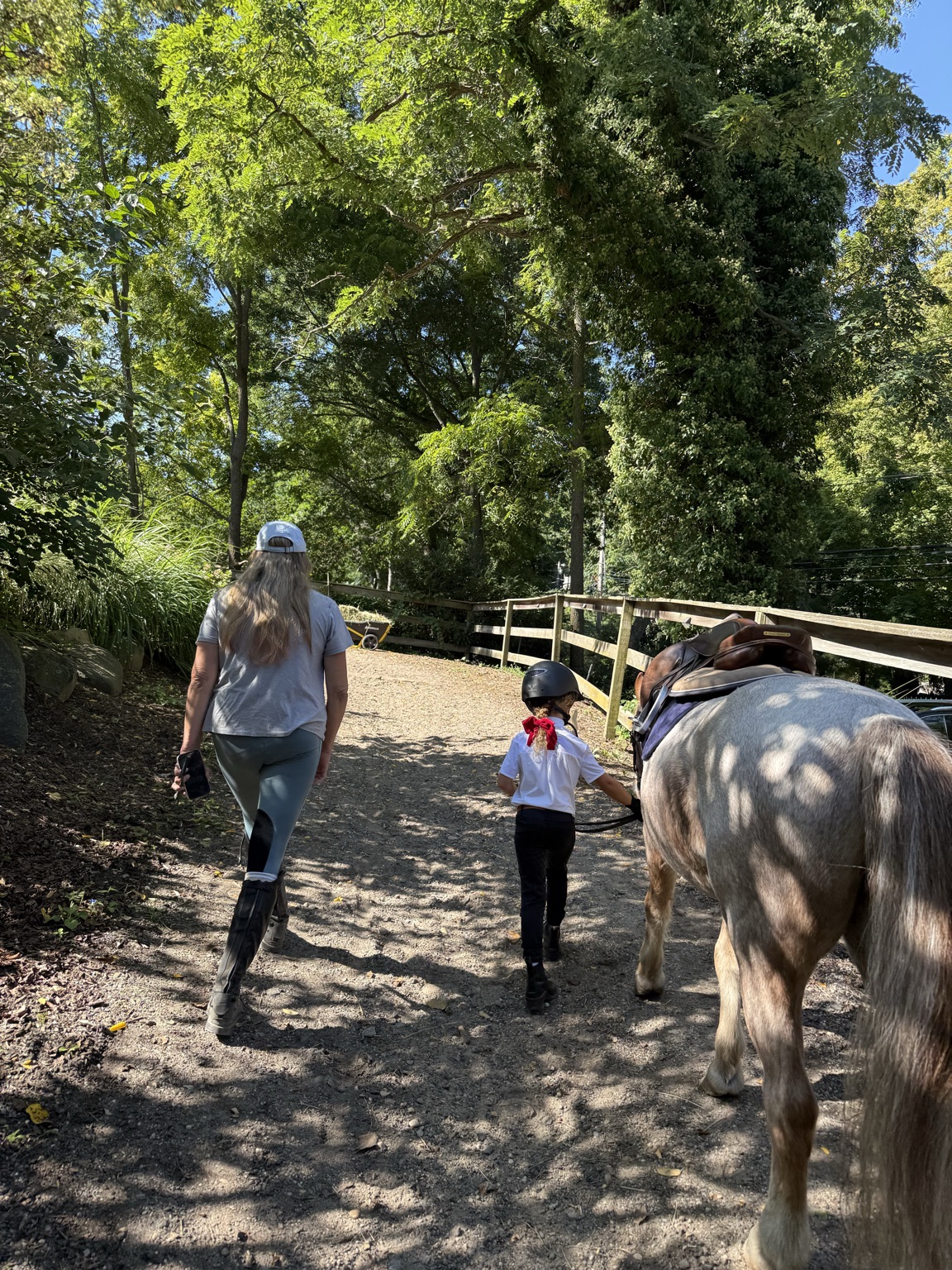 Young rider leading a saddled pony beside an adult at the barn