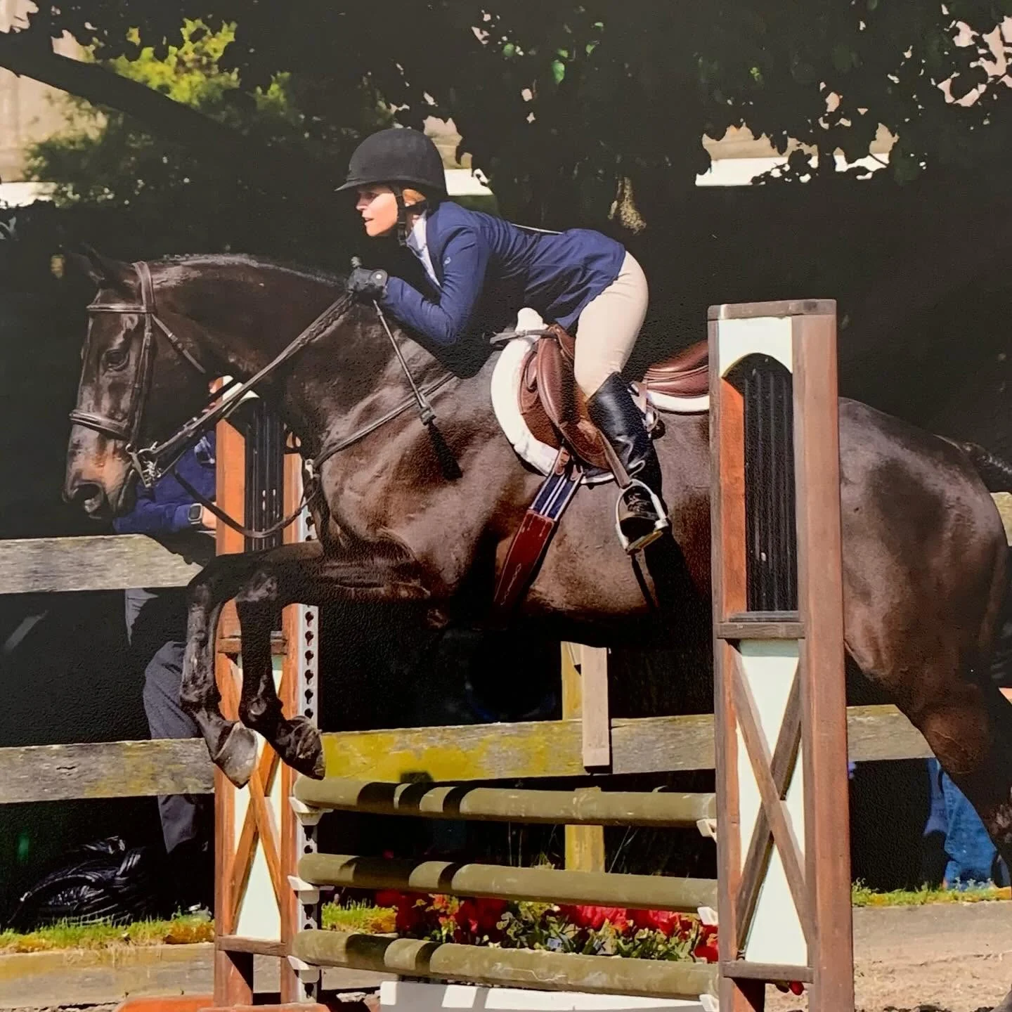 A Winding Hill Stables rider in a navy coat jumping a course at a show